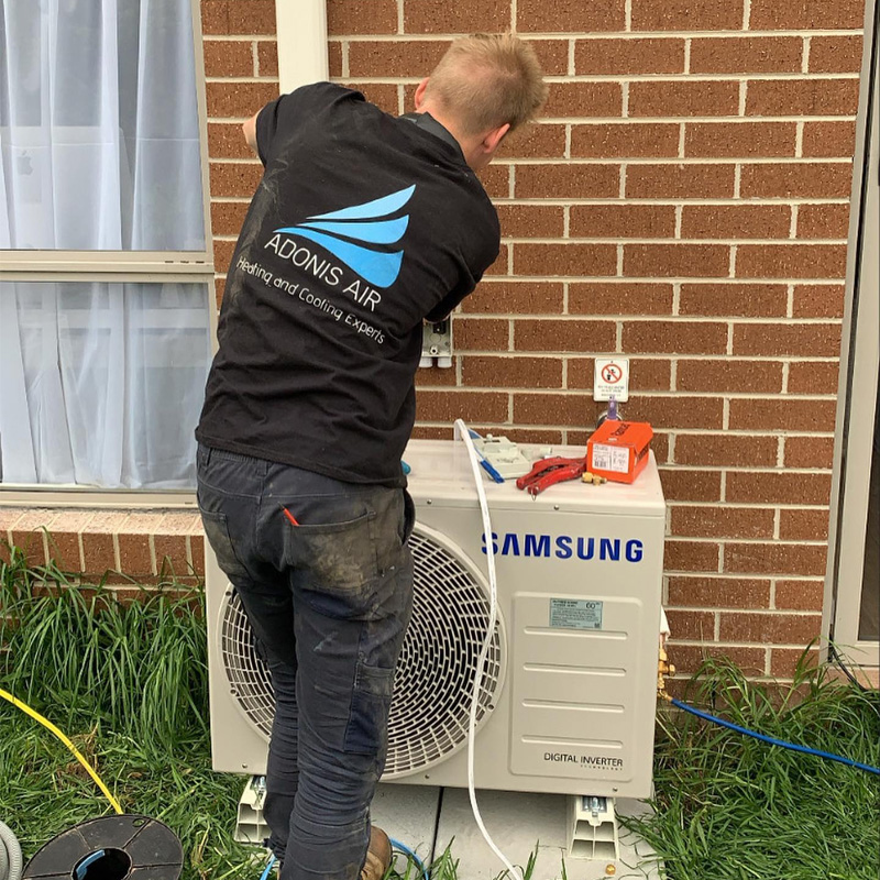 Technician working on a Samsung outdoor air conditioner beside a brick wall