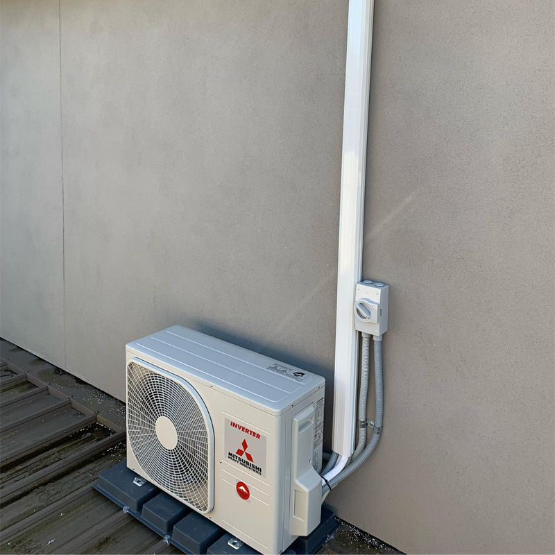 Outdoor air conditioning unit on a timber deck beside a rendered wall